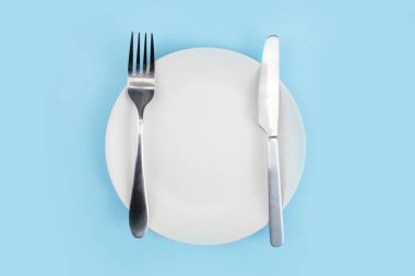 Mavi arka planda kaşığı olan beyaz bir tabak. Üst görünüm.