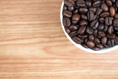 Kahverengi ahşap desenli, beyaz bardakta kahve çekirdekleri.