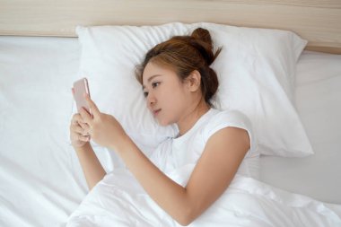Asyalı kadın akıllı telefon kullanıyor ve yatakta yatıyor..