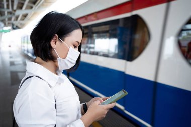 Maske takan Asyalı kadın, ülkede COVID-19 salgını, enfeksiyon kapma ve salgını meydana gelirken metro treninde bekliyor..