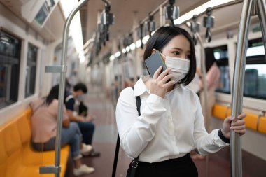 Metroda maske takan Asyalı bir kadın. O, büyük bir şehirde seyahat ederken telefonunu kullanıyor. Enfeksiyon ve salgın kavramı.