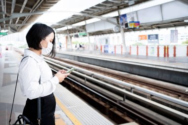 Close-up photo of Asian woman uses a smartphone while waiting for the subway. clipart