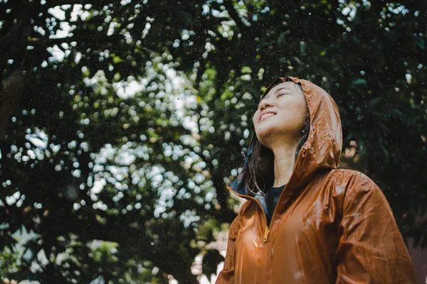 Asian woman in an orange raincoat is outdoors. She used her face to pick up the falling rain.