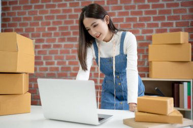 Asyalı girişimci paket ürün kutusu hazırlamak için çevrimiçi alışveriş siparişini bilgisayardan alıyor.