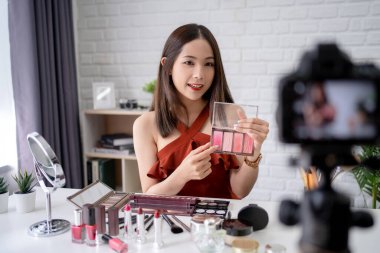 Asyalı güzel kadın blogcu kameranın önünde makyaj yapmayı ve makyaj malzemelerini kullanmayı gösteriyor..