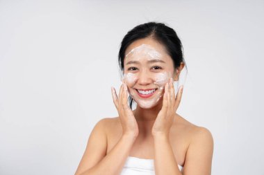 Duşta duran güzel bir Asyalı kadının yakın çekimi. Cildine temizleyici köpük sürüyor ve gülümsüyor..