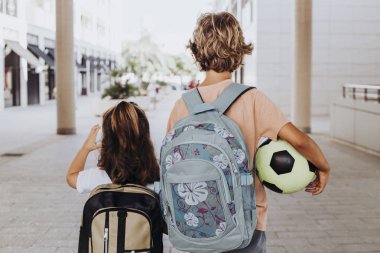 kardeşler sırt çantaları ve bir futbol topu ile okula gitmek.