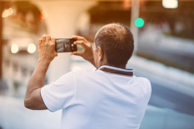 Yetişkin erkek turist, cep kamerasıyla fotoğraf çekiyor şehir manzarası, gün batımı ışığı