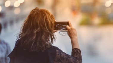 Yetişkin bir kadın turist, mobil kamerasıyla fotoğraf çekiyor. Şehir manzarası, yaz yürüyüşü, gün batımı...