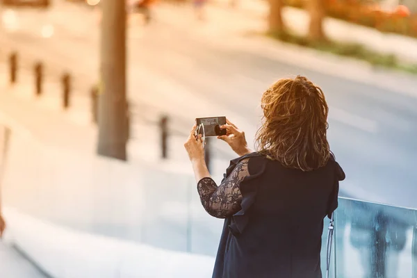 adult female tourist, photograph with her mobile camera an urban landscape, , sunset light sunset