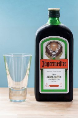 ZAGREB, CROATIA - APRIL 06, 2015:Bottle of Jagermeister on wooden table with blue background. Jagermeister is a German alcohol drink made with 56 different herbs and spices.