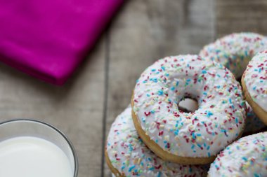 Beyaz sır ve rustik masa üzerinde renkli sprinkles ile Donuts. Sığ alan derinliği.