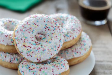 Beyaz sır ve rustik masa üzerinde renkli sprinkles ile Donuts. Sığ alan derinliği.