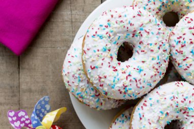 Rustik masada beyaz sır ve renkli sprinkles ile Donuts
