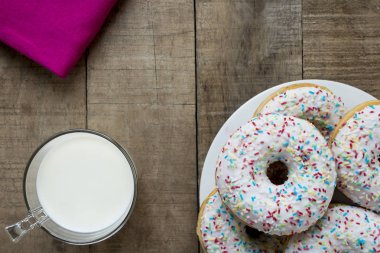 Rustik masada beyaz sır ve renkli sprinkles ile Donuts