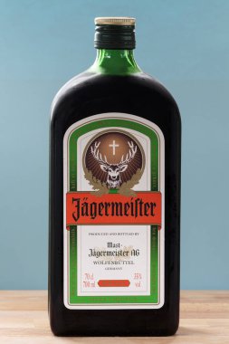 ZAGREB, CROATIA - APRIL 06, 2015: Bottle of Jagermeister on wooden table with blue background. Jagermeister is a German alcohol drink made with 56 different herbs and spices.