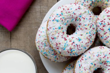 Rustik masada beyaz sır ve renkli sprinkles ile Donuts