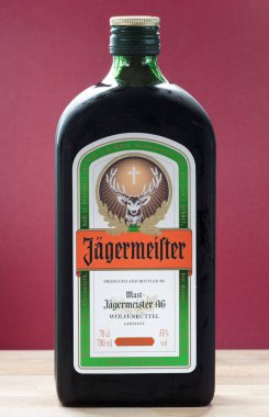 ZAGREB, CROATIA - APRIL 06, 2015:Bottle of Jagermeister on wooden table with red background. Jagermeister is a German alcohol drink made with 56 different herbs and spices.