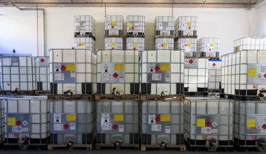 ZAGREB, CROATIA - AUGUST 08, 2014: IBC Containers with highly flammable chemical liquids in warehouse. Containers have ADR symbols of 3rd. category on it clipart