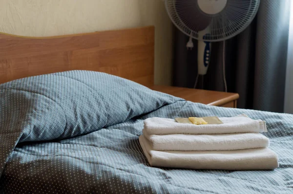 Hotel room. On the bed are three towels, soap, shampoo, shower gel.