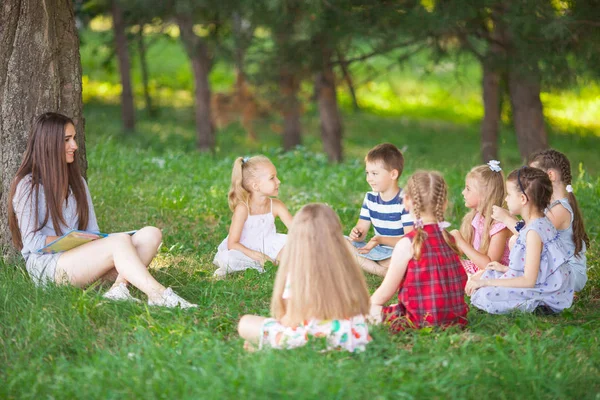 children hold a lesson with the teacher in the park on a green l