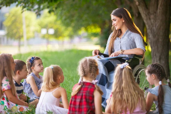 children hold a lesson with the teacher in the park on a green l
