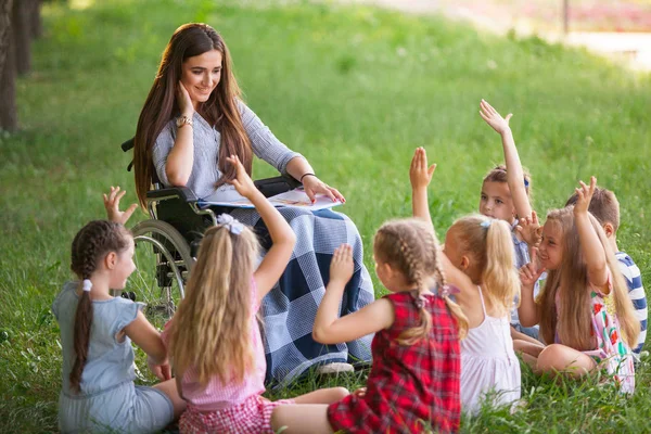 children hold a lesson with the teacher in the park on a green l