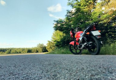 Kırmızı motosiklet ormanın yanındaki yolda tek başına duruyor.