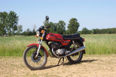 Red Honda Twin125 oldtimer motorcycle in a grassy natural background clipart