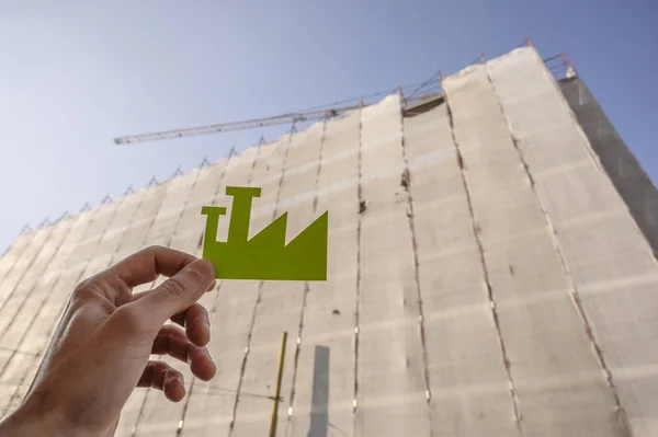 Hand holding a Green Industry sign against construction site.