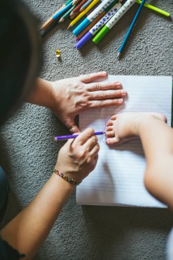 Anne renkli kalemlerle kağıdın üzerine bebek ayağı çiziyor.