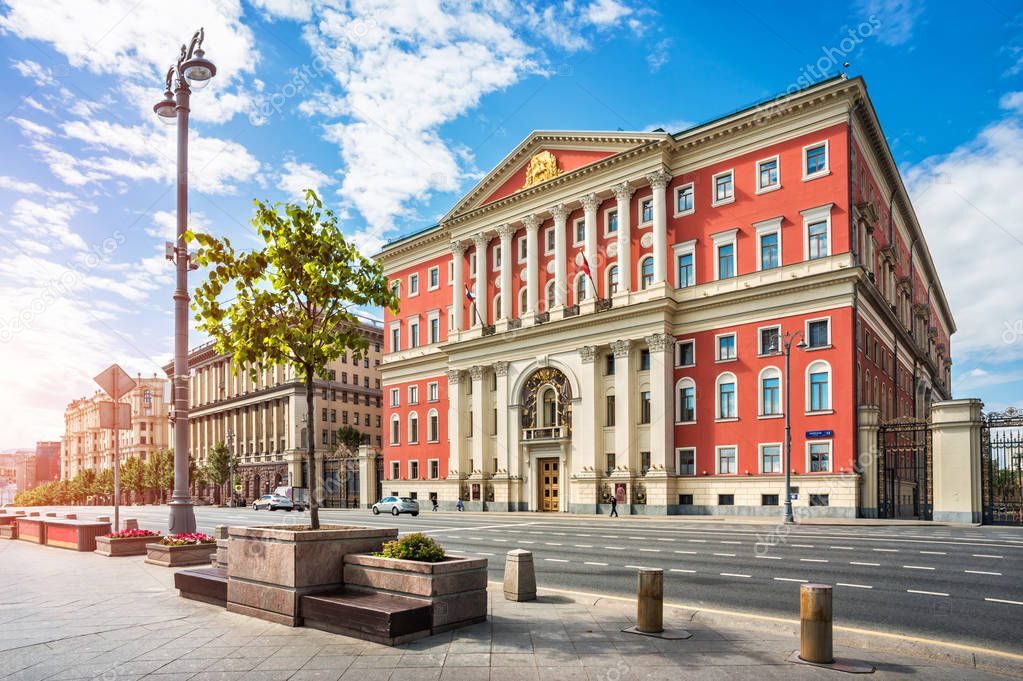 Red building of the Moscow Government on Tverskaya Street on a summer sunny morning and a green tree