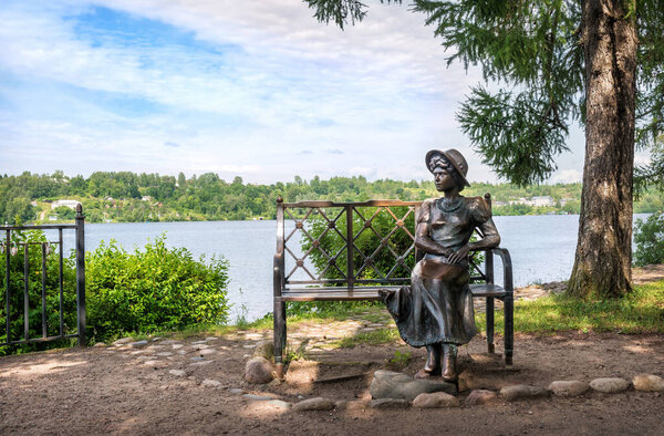 A sculpture of a summer resident girl on a bench in the town of Plyos on the Volga river embankment on a sunny summer day