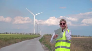 Turuncu yelek ve kravatlı kadın mühendis rüzgar jeneratörlerinin çalışmasını kontrol ediyor. Geleceğin enerjisi. Çevre Güvenliği