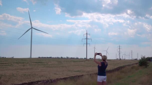 一位年轻女子在智能手机上拍摄风力发电机 — 图库视频影像