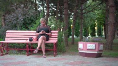 Genç bir kadın parkta dinleniyor. Bir bankta oturur ve onun akıllı telefon bakar.