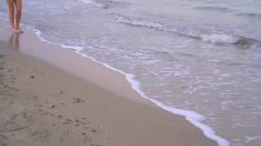 Yavaş yavaş yuvarlanan küçük dalgalar arka plan aleyhine deniz kıyısında yürüyen bir kız. Keyifli akşam esintisi.