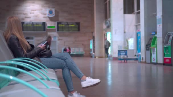 一位年轻的女游客正在车站等她的航班 她正在看她的智能手机 — 图库视频影像