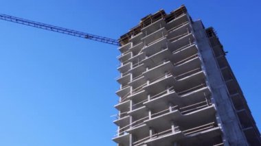 Yüksek binanın inşaat halindeki küçük bir parçası, mavi gökyüzüne karşı bir vinç. İnşaat alanındaki beton yapılar.