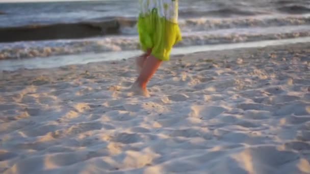 認識できない少女は 太陽の光を満たすために砂浜に沿って裸足で走ります 選択的焦点でスローモーション 海辺での休息 — ストック動画
