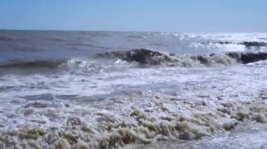 Parlak güneş ışınları azgın bir denizin ya da okyanusun yüzeyine yansıyor. Parlak ışık dalgaları kıyıya vuruyor. Fırtına rüzgarı.
