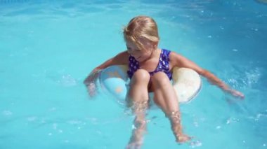 Küçük kız otel havuzunda dinleniyor. Lastik bir halkada yüzüyor ve gülümsüyor. Sıcak bir günde yüzmek.