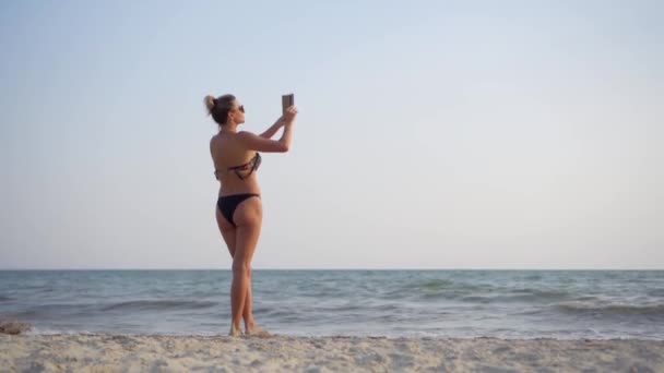 Eine junge schlanke Frau im Badeanzug macht ein Foto auf ihrem Handy für ein soziales Netzwerk. Sommerurlaub am Meer.