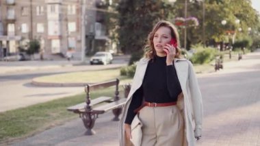 Genç ve şık bir bayan sokakta güvenle yürüyor ve telefonda konuşuyor. Modern bir kadının iş tarzı..