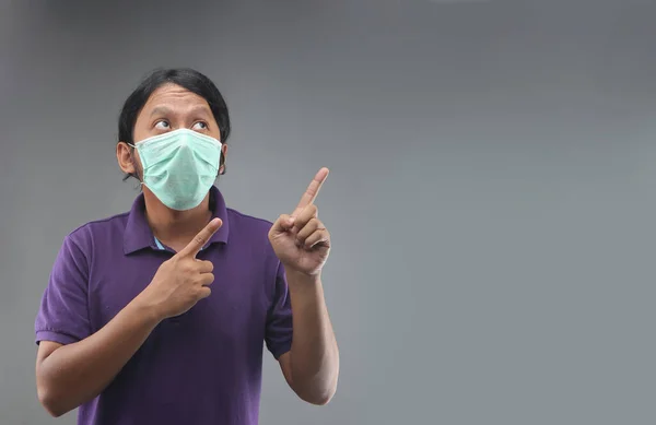 灰色の背景に隔離された顔のマスクやマスクの手の指のポインティングスペースを持つアジアの男 — ストック写真