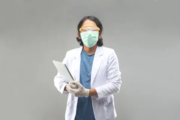 asian male doctor with face mask, gloves, googles holding tablet smartphone for information pandemic covid-2019