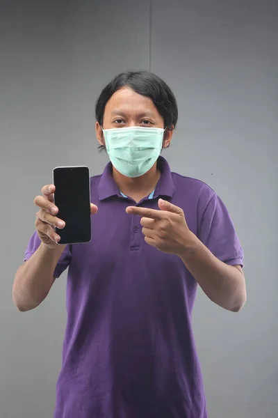 new normal man gesture hand showing blank space with smartphone and face mask for safety corona virus isolated on gray background