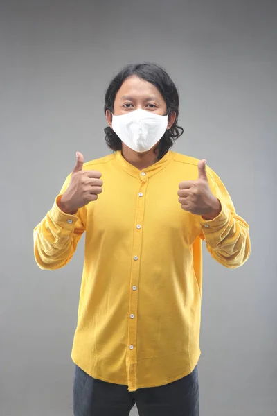 新しい普通のアジア人の男幸せな使用顔マスク用Covid 19で黄色のシャツでグレーの背景に隔離 — ストック写真
