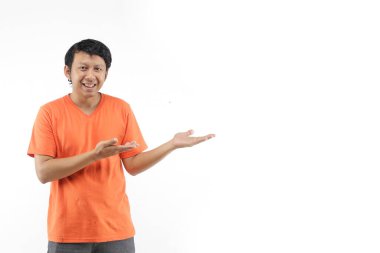 Endonezyalı genç adam gülümsüyor ve turuncu tişörtle boş alan gösteriyor.