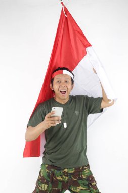 Endonezyalı asker akıllı telefon kullanıyor ve elinde kırmızı beyaz bayrak tutuyor.